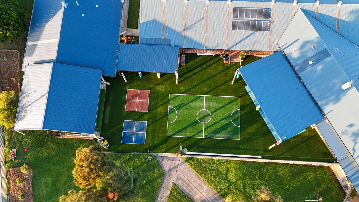 Aerial view of a synthetic grass soccer field and handball courts between school buildings